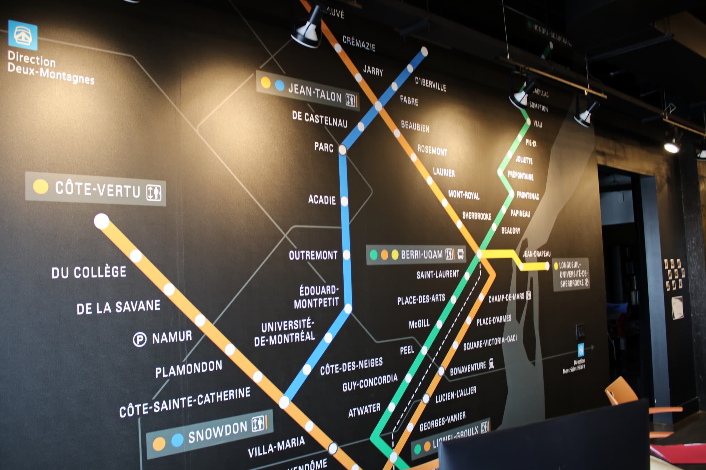 Carte du métro de Montréal peinte en grand sur un mur noir du bureau, ses lignes orange, verte, bleue et jaune au complet.