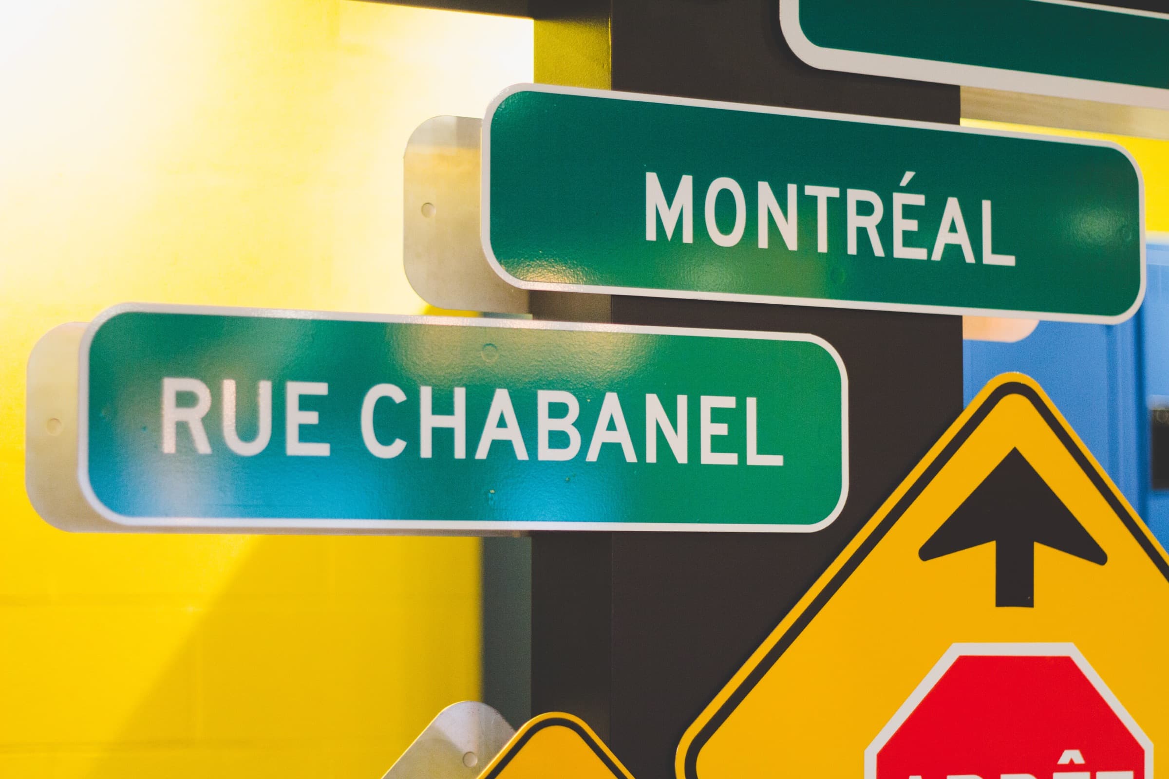 Gros plan sur deux plaques de rue vertes, « Montréal » et « Rue Chabanel », devant un mur jaune vif.